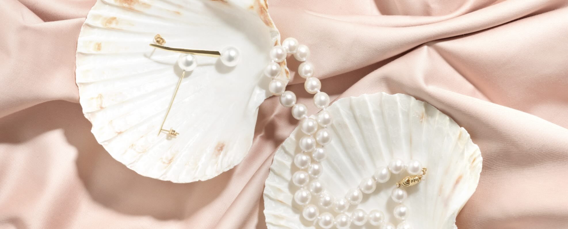 White pearl jewelry arranged on oyster shells and pink satin.