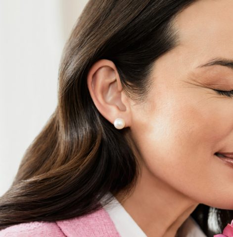 A close up of a woman wearing a simple pearl stud earring.