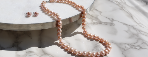 Pink pearl necklace and matching earrings displayed on marble
