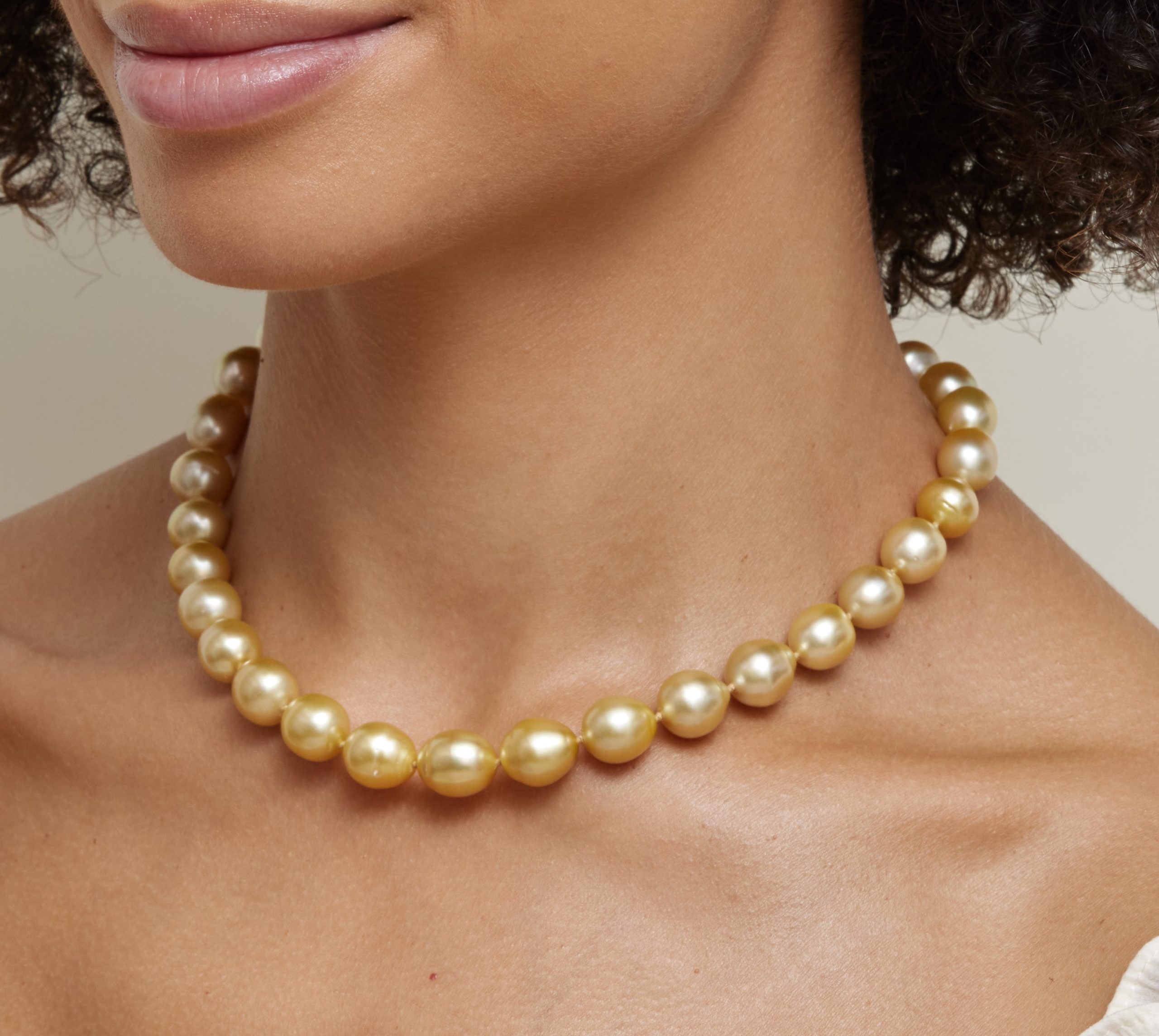A close up of a woman wearing a lustrous Golden South Sea pearl necklace, with strong uniformity.
