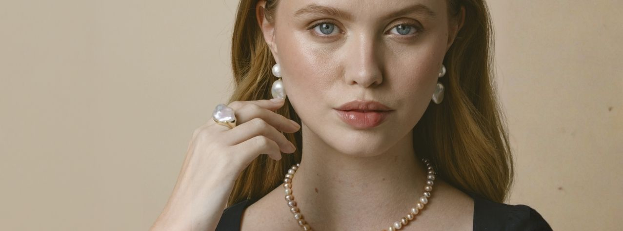 A young woman wearing stylish baroque pearl drop earrings, a matching ring, and chic pearl srand necklace.