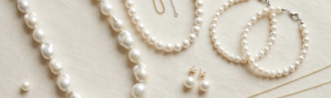 A flatlay image of pearl jewelry of different types and styles laying on top of a cream linen background.