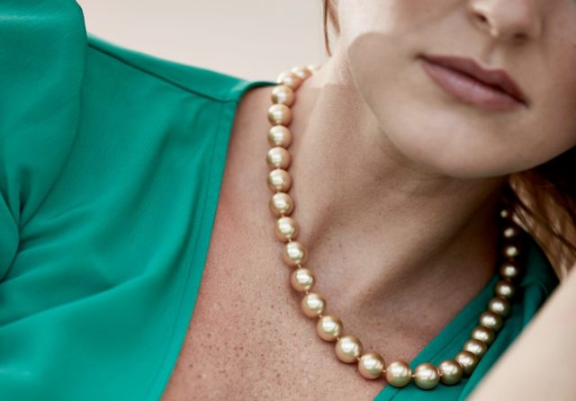 Close-up of a woman wearing a golden pearl necklace, paired with an emerald green top.