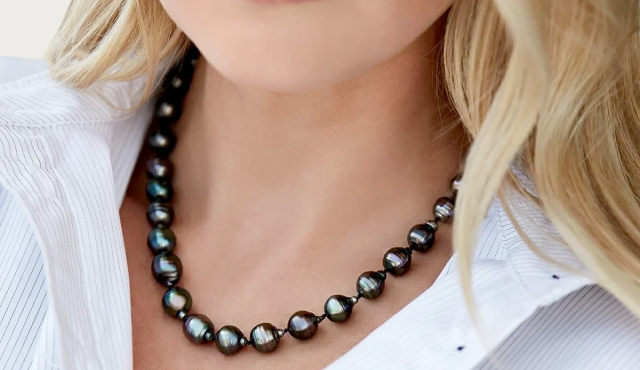 Close-up of a woman wearing a dark, iridescent pearl necklace over a white striped shirt.