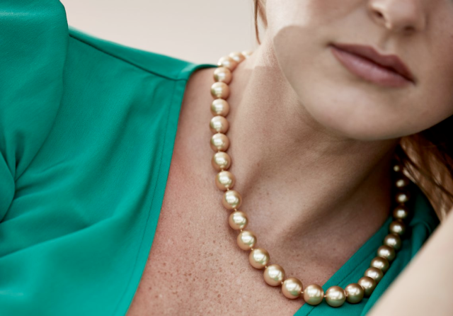 Close-up of a woman wearing a golden pearl necklace, paired with an emerald green top.