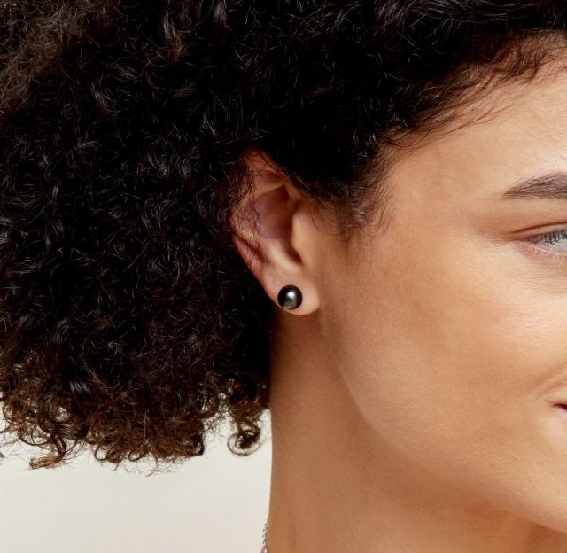 A closeup image of a woman wearing a black Tahitian pearl stud earring.