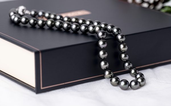 A strand of black pearls draped across a stylish gift box.