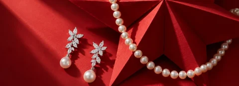 Pearl drop earrings with sparkling floral clusters beside a white pearl strand, set against a folded red paper star.